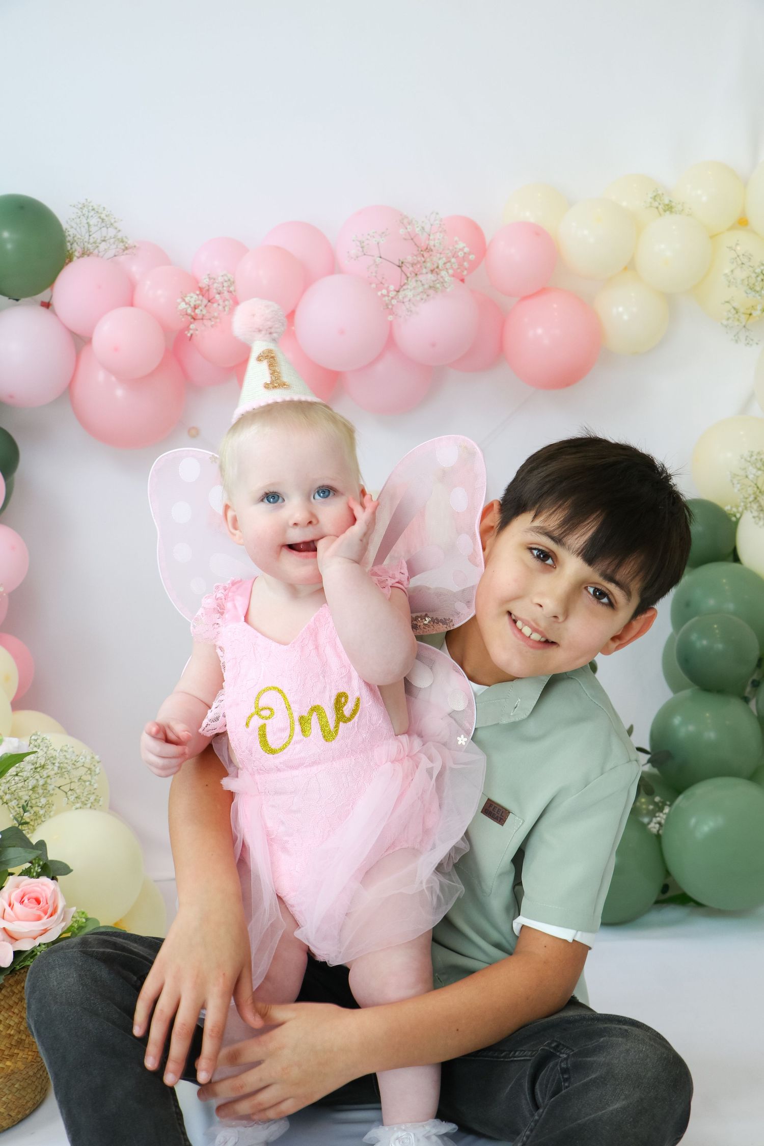 Baby in pink tulle dress with floral headband poses against white balloon backdrop. Coventry Cake Smash Photographer. First Birthday.