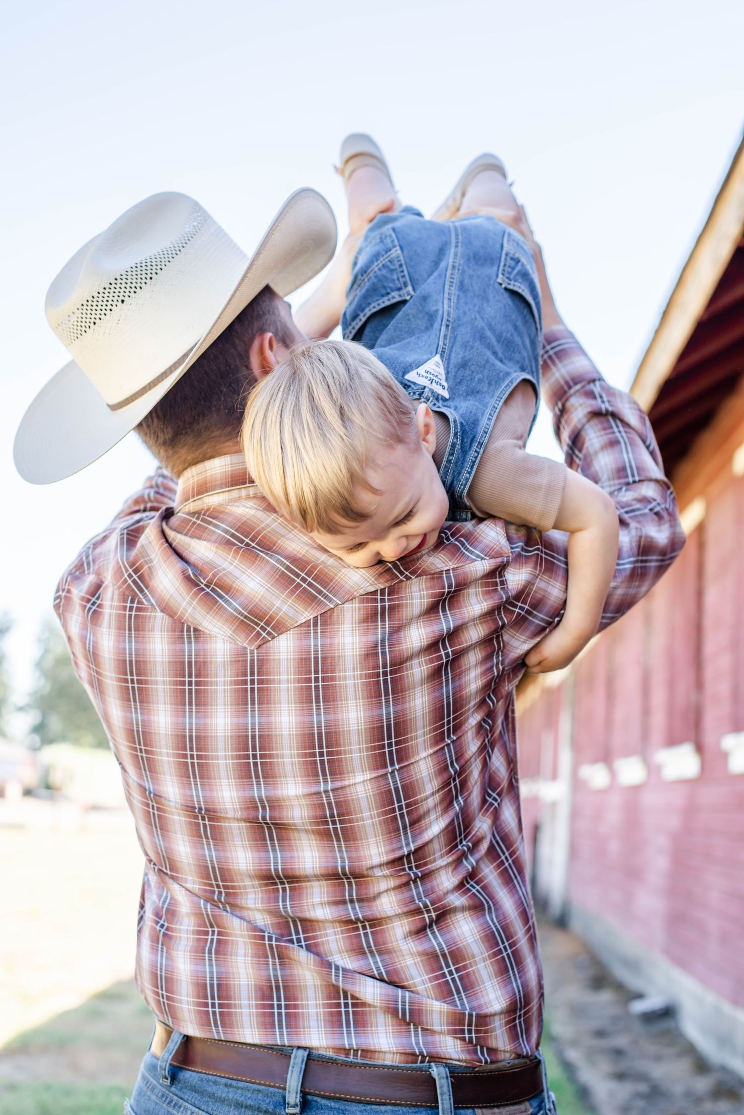 A loving embrace captured against a rustic red barn background during a family photoshoot.
