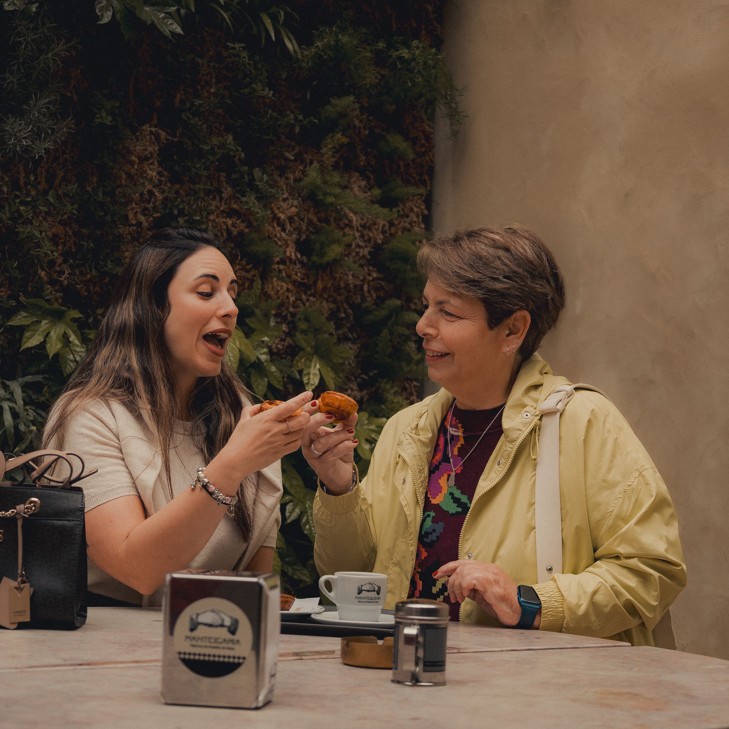 Two friends sharing food and coffee at outdoor table.
