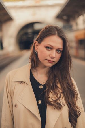 Portrait of woman in beige trench coat at train station.