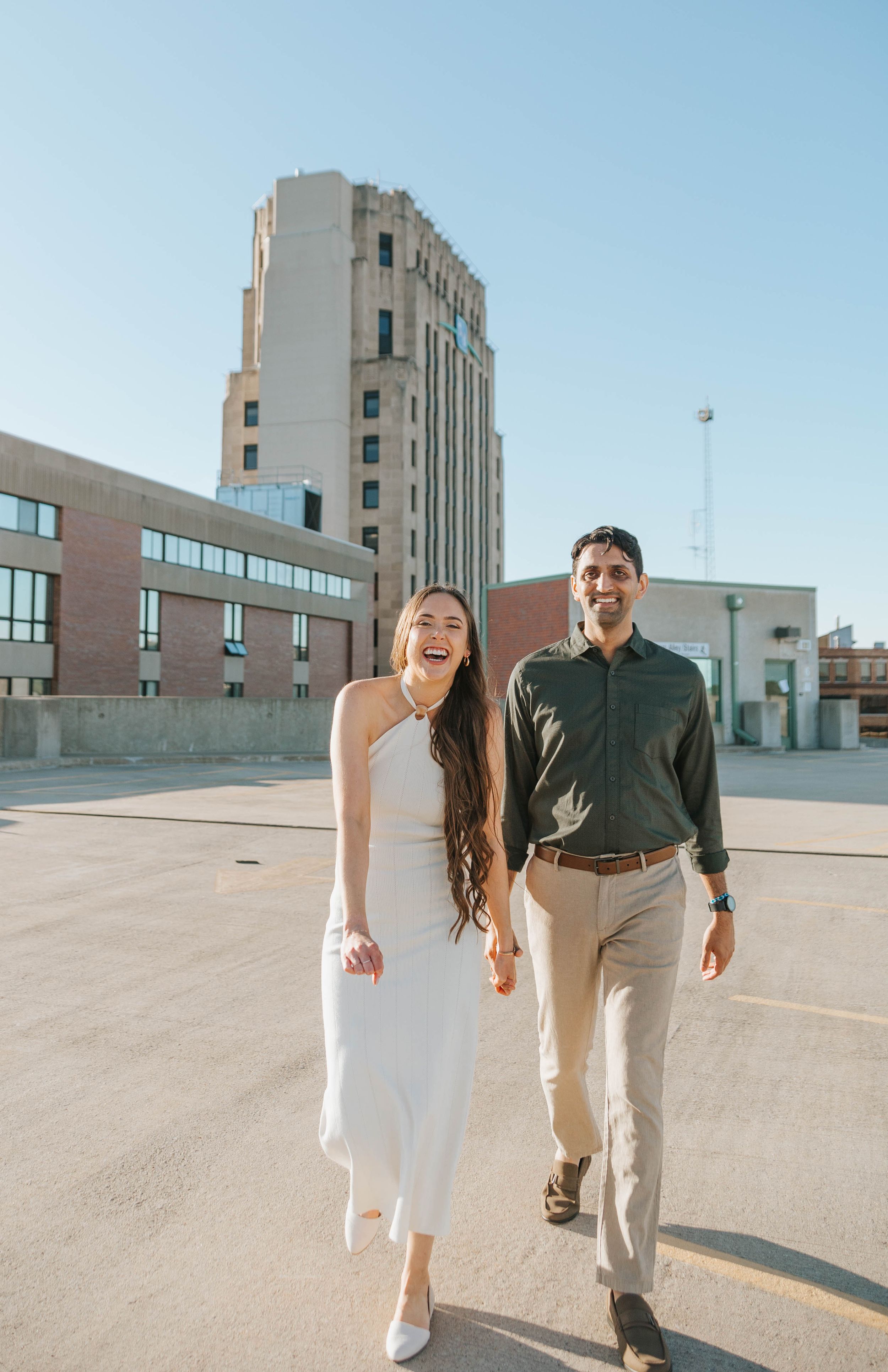 A couple takes a romantic stroll on a rooftop parking area on a sunny day.