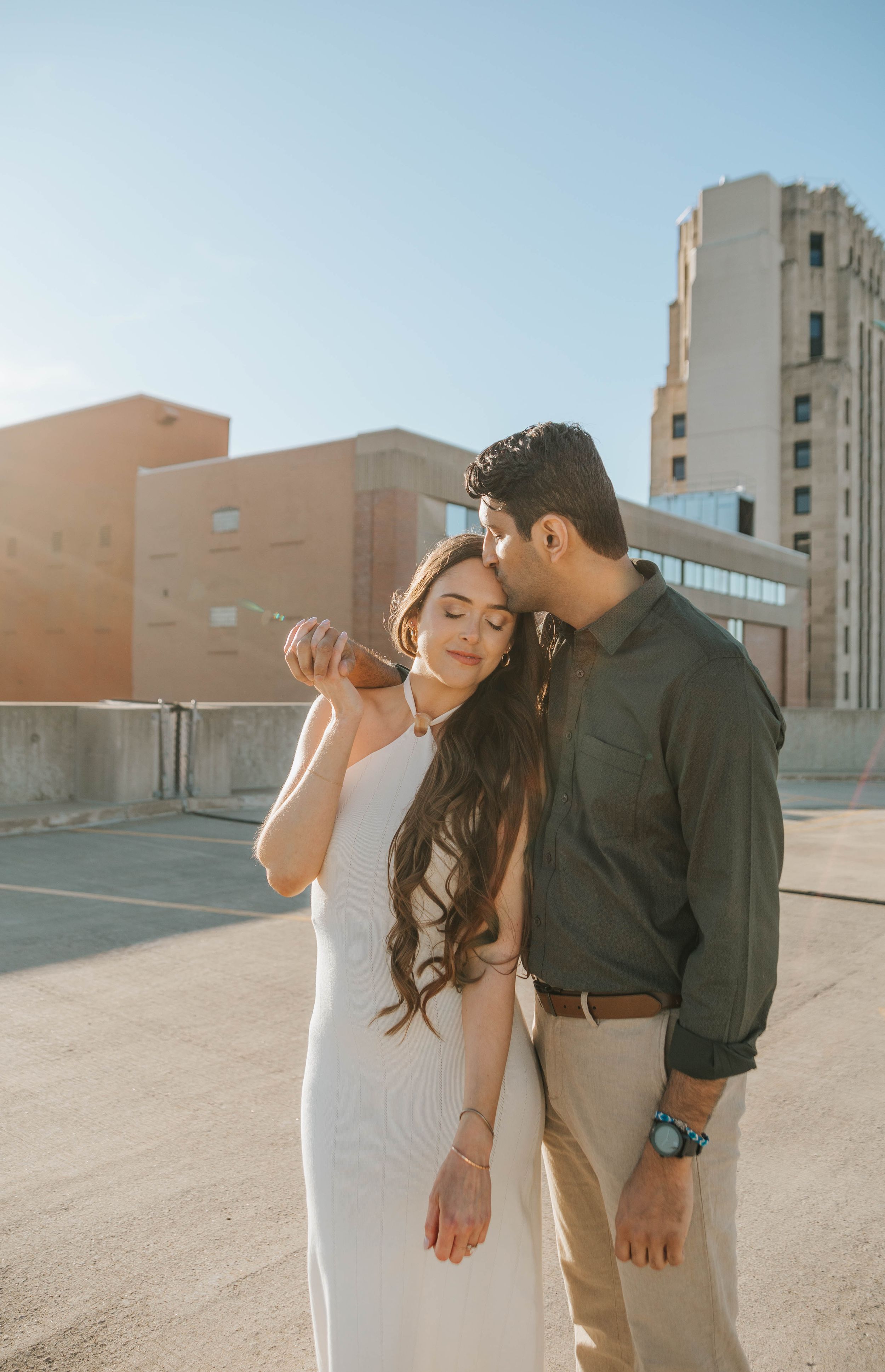 A couple in white and dark clothing shares an intimate moment on an urban rooftop.