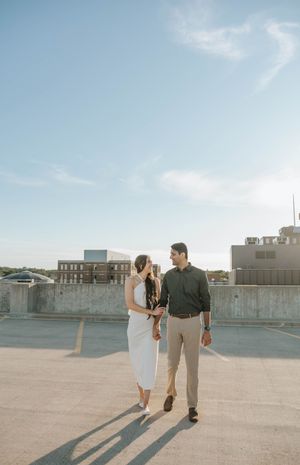 A couple casts long shadows while dancing on a sunny rooftop in an urban setting.