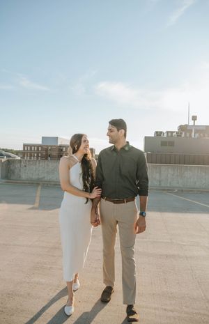 A couple in contrasting outfits walks hand in hand across an empty rooftop.