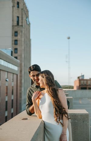A couple shares laughter while leaning against a concrete wall on a rooftop.