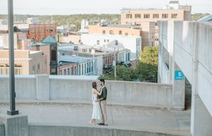 A couple shares an intimate moment on a rooftop overlooking a cityscape at dusk.