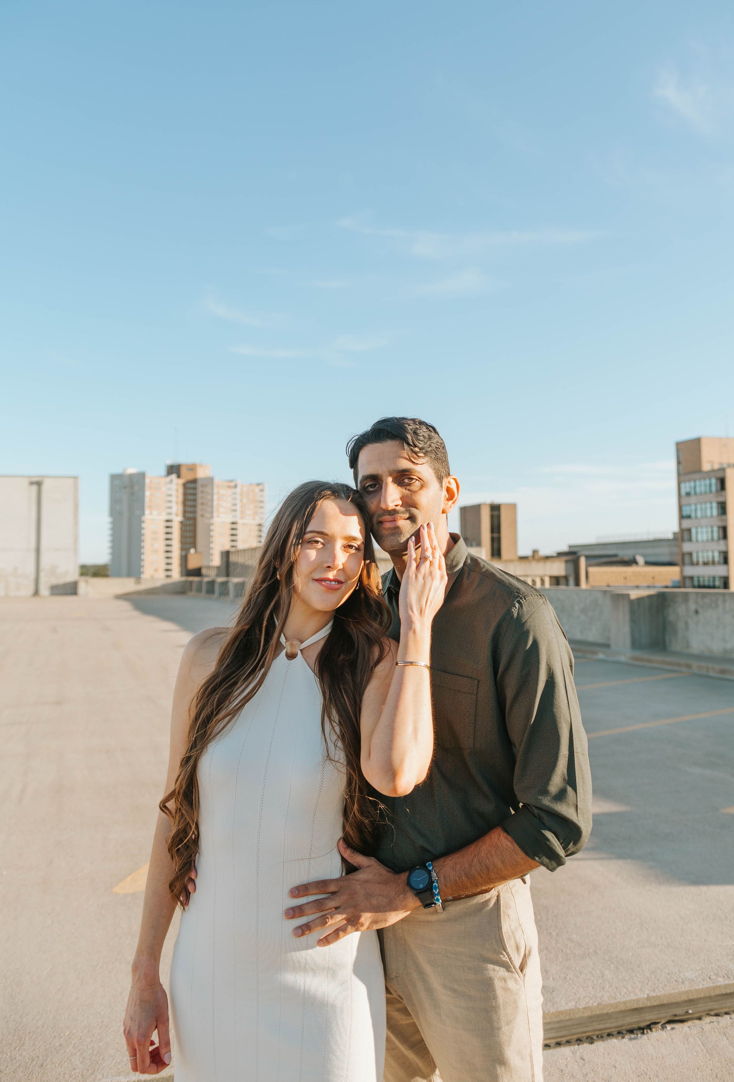 A couple poses together on an urban rooftop with city buildings in the background.