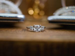 A sparkling diamond engagement ring sits on a wooden surface with a blurred bokeh background.