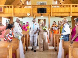 A wedding celebration in a rustic wooden chapel with guests seated in pews decorated with white fabric and flowers.