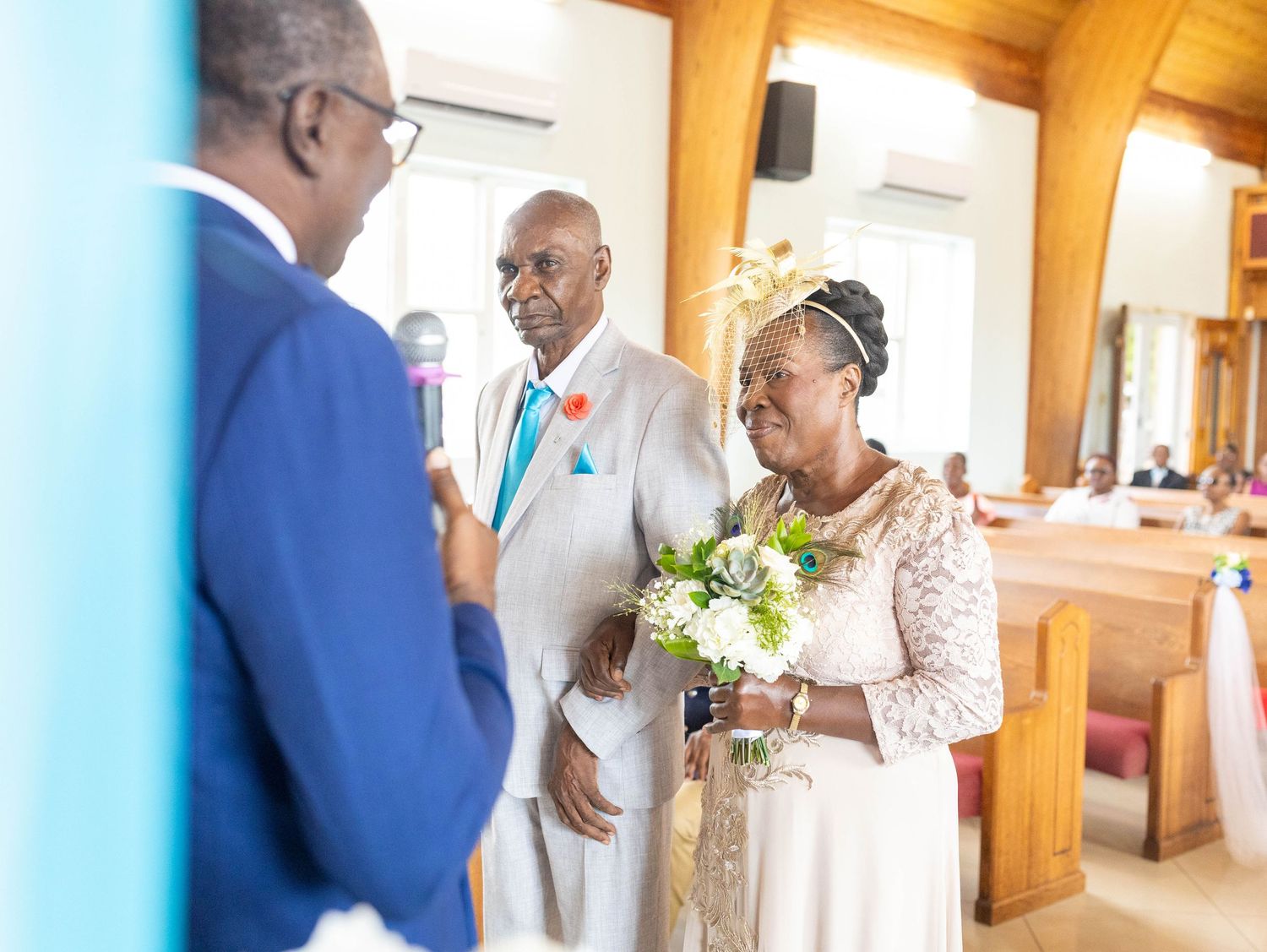 A senior couple in formal wedding attire stands together inside a church as they exchange vows during a ceremony.