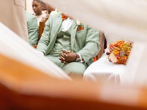 Wedding party members in matching mint green suits sit beside a vibrant orange floral bouquet.