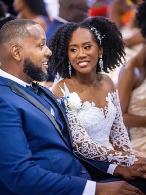 A couple shares a joyful moment at their wedding, the bride in lace gown with hair accessory and groom in royal blue suit.