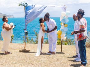A small outdoor wedding ceremony takes place on a scenic cliffside overlooking bright blue ocean waters.