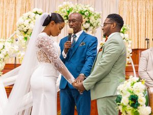 Bride and groom share an intimate moment at the altar with officiant during wedding ceremony with floral backdrop.