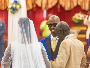 A couple stands at a wedding ceremony altar with a minister wearing sunglasses in a church setting.