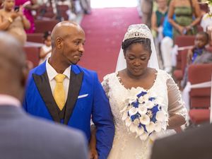 A couple during their wedding ceremony, with the bride holding a blue and white bouquet and groom wearing a royal blue suit.