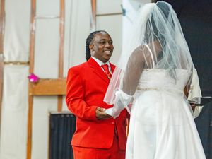 A joyful moment during a wedding ceremony with someone in a bright red suit standing with the bride in her white gown and veil.