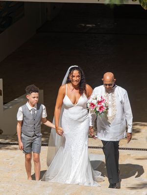 Wedding party members wearing white and gray outfits walking together joyfully on a stone path during outdoor celebration.