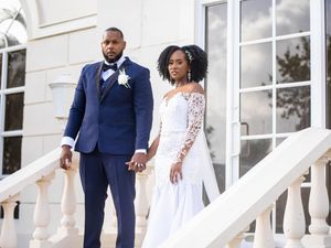 A wedding couple stands on a white porch with elegant columns at their outdoor ceremony.