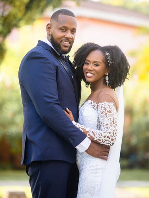 A happy couple in wedding attire pose together outdoors with a natural blurred background.
