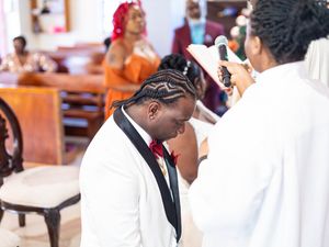 A person in a white suit jacket bows their head during what appears to be a religious ceremony in a church setting.