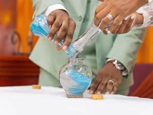 Hands pouring blue liquid chemicals from test tubes into a glass flask during a laboratory experiment.