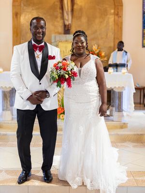 Beautiful wedding ceremony in a church with a couple in white and black formal attire holding red and pink floral bouquet.