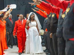 A wedding celebration with red and orange clad attendees forming an honor guard as the couple walks down the aisle.