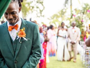 Wedding guest wearing a green three-piece suit with orange bow tie and boutonniere at an outdoor celebration.