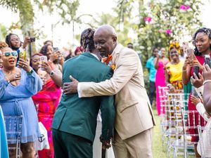 Two people share an emotional embrace at an outdoor wedding ceremony as guests look on and celebrate the moment.