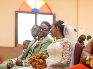 Couple in church sitting on pews during a wedding ceremony with orange floral bouquets.