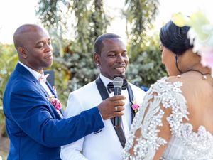 Wedding ceremony with best man holding microphone as couple exchanges vows under willow trees outdoors.
