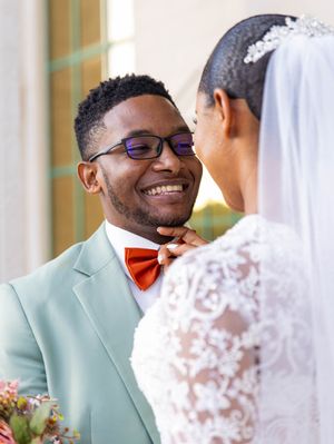 Tender wedding moment with couple wearing mint green suit and lace gown exchanging smiles during celebration.