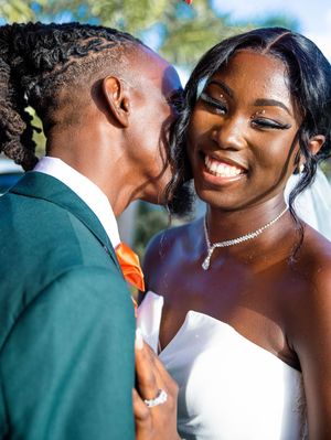 Two wedding guests share a joyful moment in formal attire, with one wearing an emerald green suit and orange tie.
