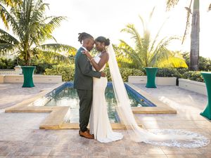 A romantic couple embraces on a tropical patio with palm trees and a long flowing veil in the golden sunlight.