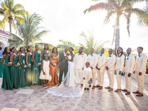 Wedding party poses on sandy beach at sunset in tropical paradise with palm trees in the background.