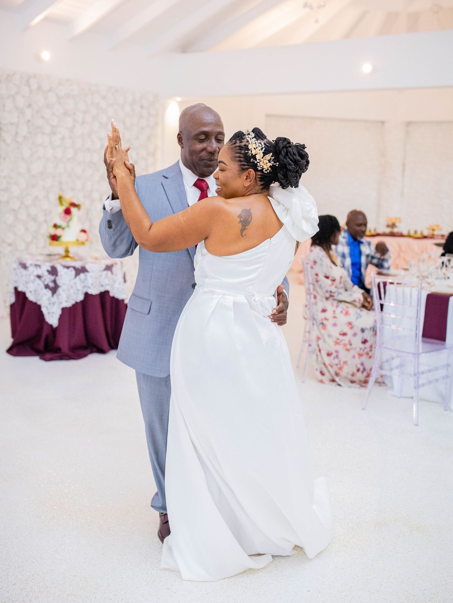 A couple dancing together at their wedding reception in a white decorated venue with burgundy table settings.