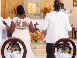 A couple kneels at the altar during a church wedding ceremony with floral decorations and chairs adorned with flowers.