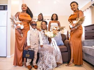 A wedding party group in rust-colored dresses and formalwear poses together indoors with bouquets.