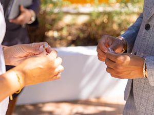 Close-up of hands during outdoor wedding ceremony with natural lighting filtering through trees.