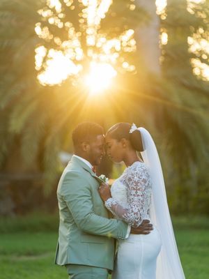 A couple shares an intimate moment at sunset in a garden as golden sunlight streams through trees behind them.