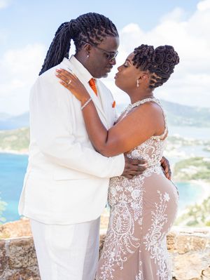 A romantic couple in white attire embraces on a scenic coastal overlook during their wedding photoshoot.
