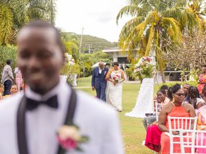An outdoor wedding ceremony setup in a tropical garden with palm trees and white chairs arranged on a lawn.