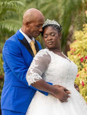 A couple shares a tender moment in their wedding attire, with the bride in white lace and groom in bright blue suit.