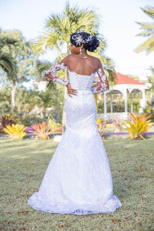 Back view of a bride in a lace mermaid wedding gown with long sleeves standing in a tropical garden setting.