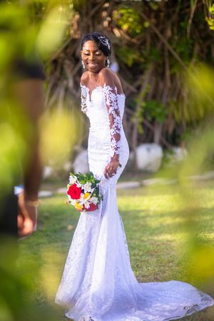 Beautiful white lace wedding gown with long sleeves and mermaid silhouette photographed outdoors with colorful bouquet.