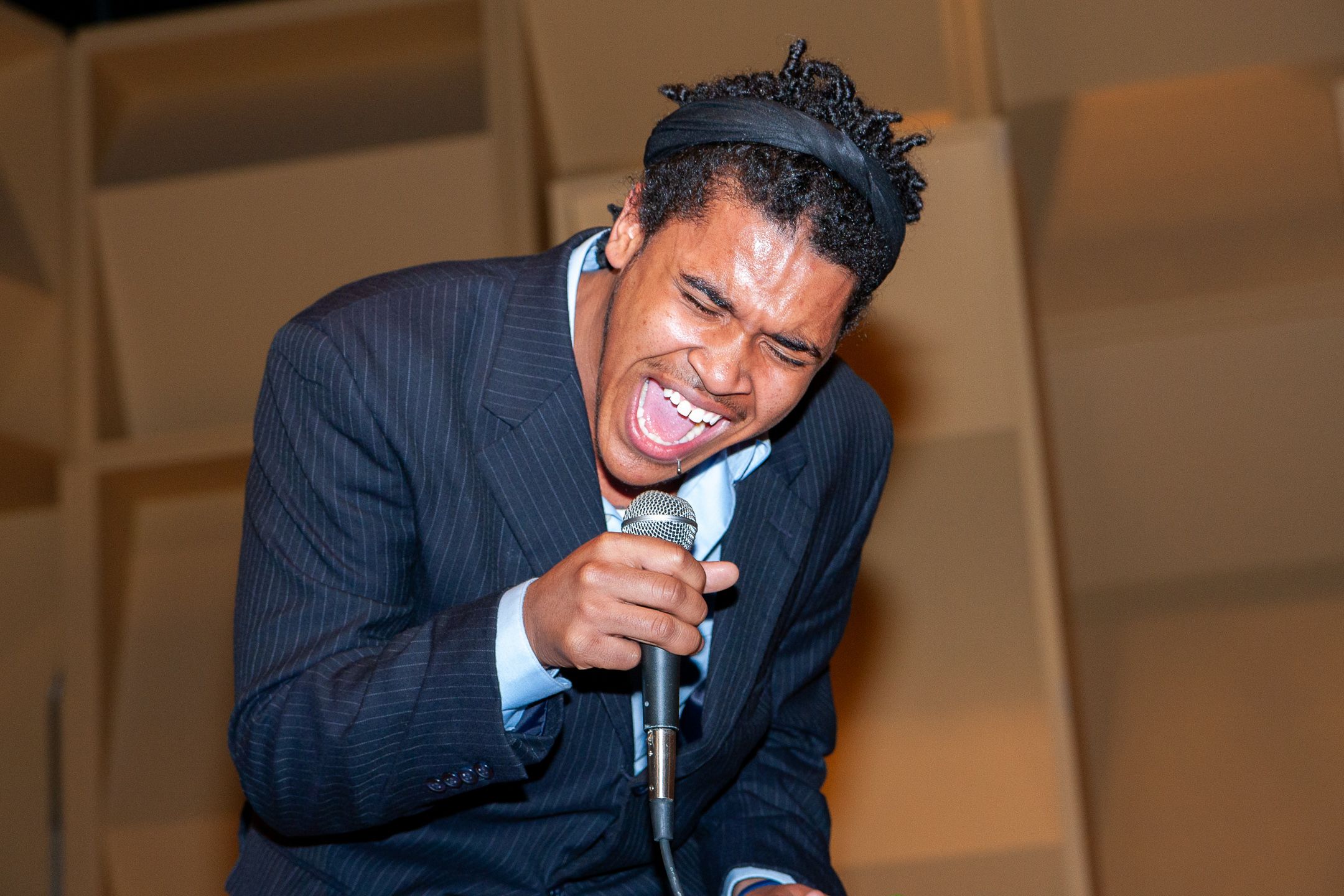 Performer in pinstriped suit clutches microphone while singing passionately on stage with animated expression.