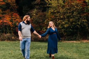 Couple laughing together in field with autumn trees.