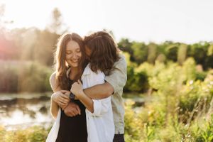 Couple laughing together by lakeside during golden hour.