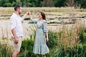 Couple dancing playfully by pond with cattails and summer greenery.